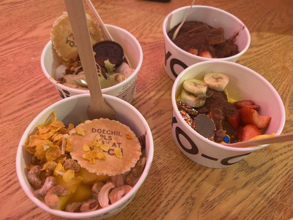 YO-CHIのカップが4つ。バナナ、いちご、チョコの粉、クッキーなどトッピングいろいろ